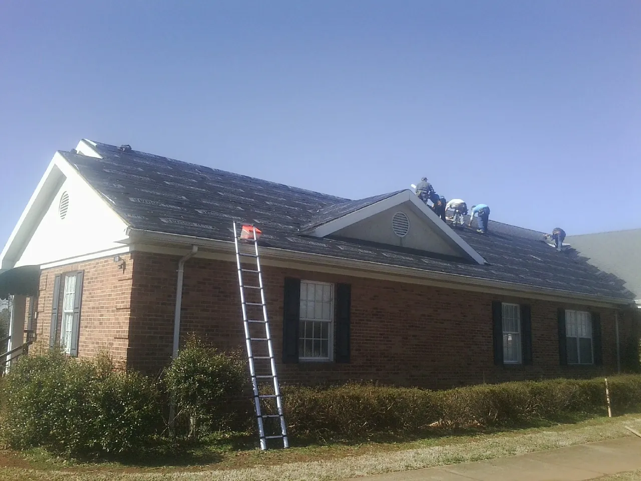 Crew tearing shingles off a brick ranch roof with a ladder set — Metal Roof Repair work by our crew in Beechmont