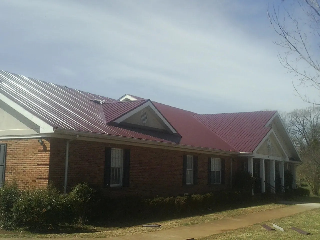 Red metal roof with gabled entries on a long brick building, from a Hail Damage Roof Repair job in Beechmont