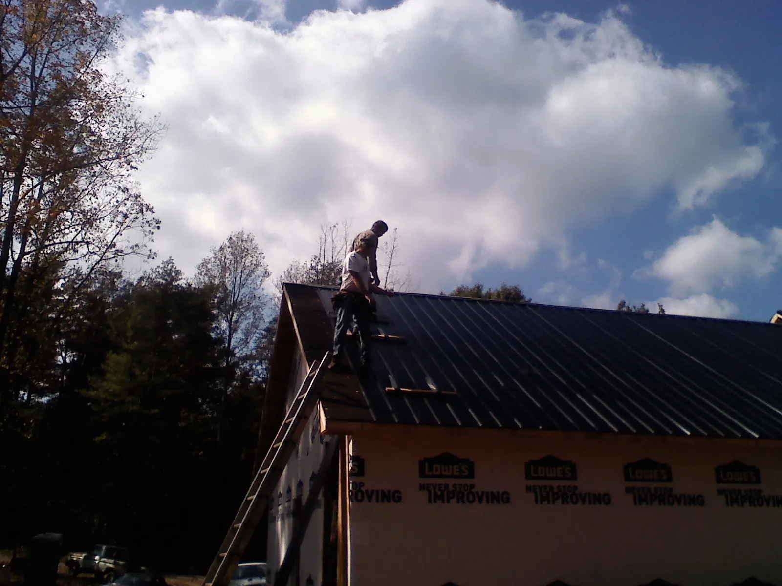 Roofer fastening dark metal panels high against a cloudy sky, from a Roof Inspection job in Beechmont