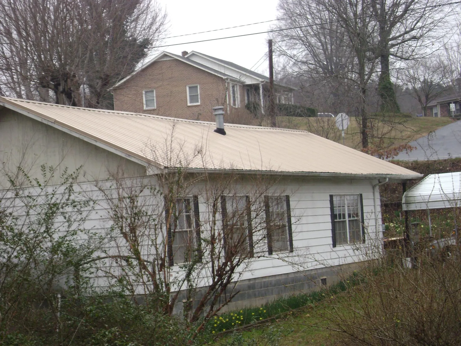 Tan metal roof on a white sided house set into a hillside — Commercial Roofing by Roofing Brothers in Beechmont